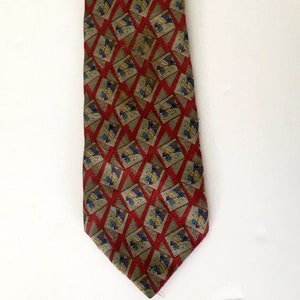 May include: A patterned necktie featuring a repeating geometric design. The tie has a red background with a diamond pattern in a lighter shade of red. Within each diamond are smaller squares with a floral pattern in shades of blue, yellow, and purple.