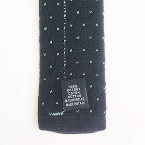 Puede incluir: Primer plano de una corbata de punto azul marino con peque&ntilde;os patrones en forma de V de color azul claro. La etiqueta de la corbata dice "100% COTONE COTON COTTON BAUMWOLLE MADE IN ITALY".