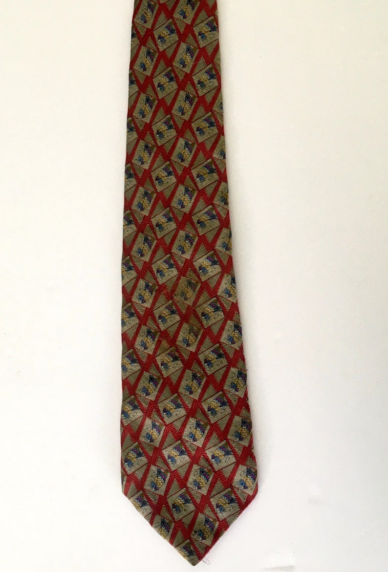 May include: A patterned necktie with a repeating geometric design. The tie features a red diamond pattern with a tan background and accents of blue and yellow. The tie is displayed against a white background.
