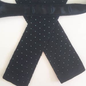 Puede incluir: Una corbata negra de punto con reverso de sat&eacute;n. La corbata presenta un patr&oacute;n texturizado de peque&ntilde;os puntos azul claro. La corbata se muestra sobre un fondo blanco.