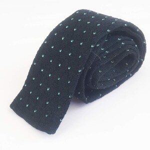 Puede incluir: Una corbata de punto azul marino enrollada con peque&ntilde;os patrones en forma de V de color azul claro, espaciados uniformemente. La corbata est&aacute; hecha de una tela texturizada y se muestra sobre un fondo blanco.