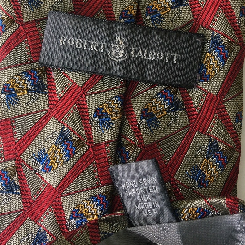 May include: Close-up of a silk tie with a geometric pattern in red, beige, blue, and yellow. The label reads "ROBERT TALBOTT" and "HAND SEWN IMPORTED SILK MADE IN U.S.A."