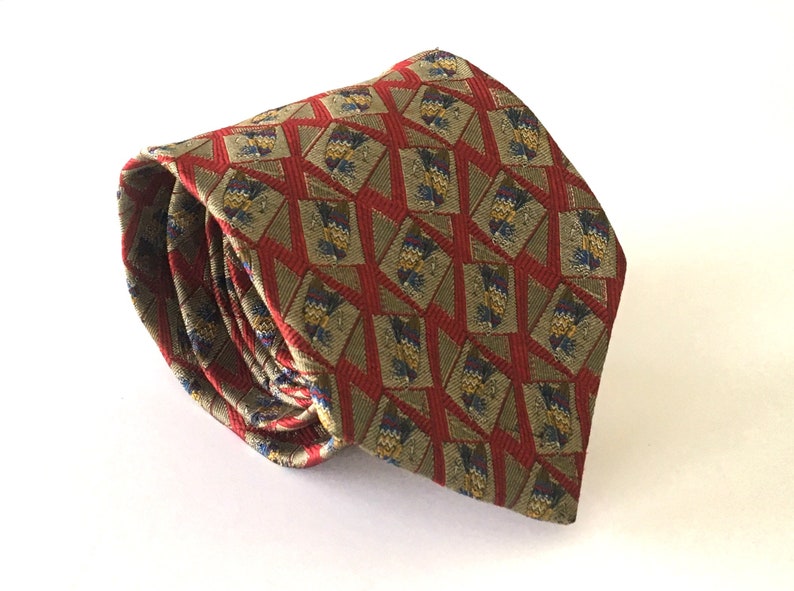 May include: Rolled-up necktie with a geometric pattern. The tie features a repeating design of olive green, red, and blue shapes. The tie is made of a woven fabric and is suitable for formal or business attire.