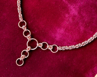 May include: A rose gold chain necklace with a Y-shaped pendant made of interconnected rings.