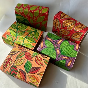 May include: Five cardboard boxes with colorful leaf designs. The boxes feature various patterns in red, green, orange, yellow, and purple. The leaves are hand-drawn, adding a unique, artistic touch to each box.