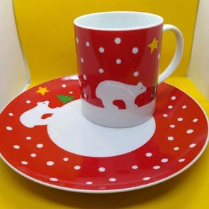 Peut inclure: Un ensemble tasse et assiette en céramique rouge sur le thème de l'hiver. La tasse et l'assiette présentent un motif d'ours polaire blanc, des pois blancs et une étoile jaune. L'assiette mesure environ 20 cm de diamètre.