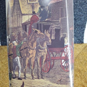 May include: A red container with a detailed illustration of a horse-drawn carriage, people, and buildings. The text "Johnnie Walker" is at the top. The scene is set in a rural environment with chickens.