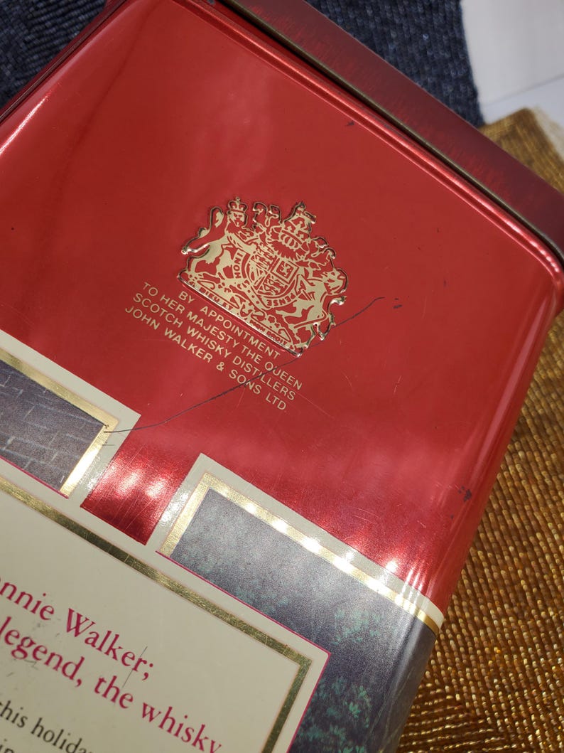 May include: A red rectangular tin with gold trim and text. The tin features a gold emblem and the text "BY APPOINTMENT TO HER MAJESTY THE QUEEN SCOTCH WHISKY DISTILLERS JOHN WALKER & SONS LTD".