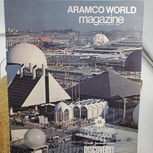 Puede incluir: Una edición vintage de la revista Aramco World de julio-agosto de 1970. La portada presenta una colorida vista aérea de un gran complejo con cúpulas, pirámides y otras estructuras arquitectónicas. El texto en la portada dice "ARAMCO WORLD magazine" y "THE ARABS AT OSAKA".