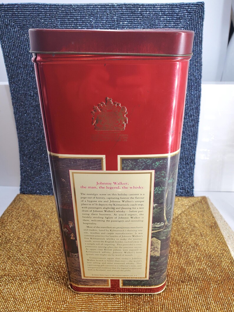 May include: A red rectangular tin with a gold emblem and text. The tin features a nostalgic scene with text that reads "Johnnie Walker: the man, the legend, the whisky." The tin is likely for storing whisky.