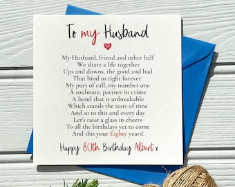 May include: A white greeting card with the text "To my Husband" and a poem, presented with a blue envelope. The card is for an 80th birthday, with the name "Albert" at the bottom. The card is on a white wooden surface.
