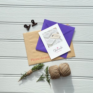 May include: An overhead shot shows a collection of stationery items. A white card with the text "Shmuncki Poem Gifts" is layered over a purple envelope and a brown envelope with the text "Please do not". Twine, rosemary, and two small clips complete the arrangement.