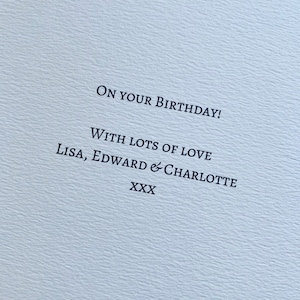 May include: A light blue card with the message "ON YOUR BIRTHDAY!" printed in black. The card also includes the text "WITH LOTS OF LOVE Lisa, Edward & Charlotte XXX". The card has a textured surface.