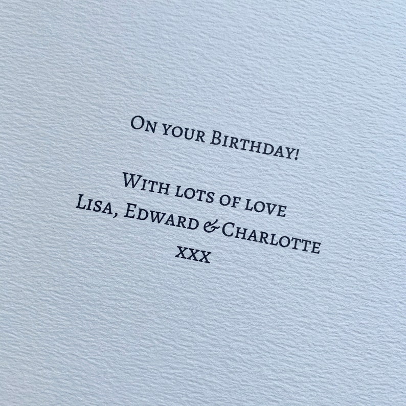 May include: A light blue card with the message "ON YOUR BIRTHDAY!" printed in black. The card also includes the text "WITH LOTS OF LOVE Lisa, Edward & Charlotte XXX". The card has a textured surface.