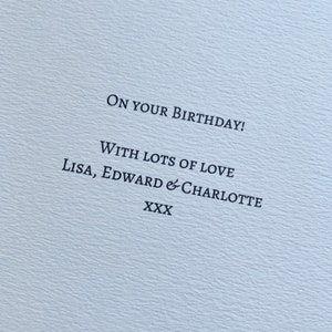 May include: A light blue card with the message "ON YOUR BIRTHDAY!" printed in black. The card also includes the text "WITH LOTS OF LOVE Lisa, Edward & Charlotte XXX". The card has a textured surface.