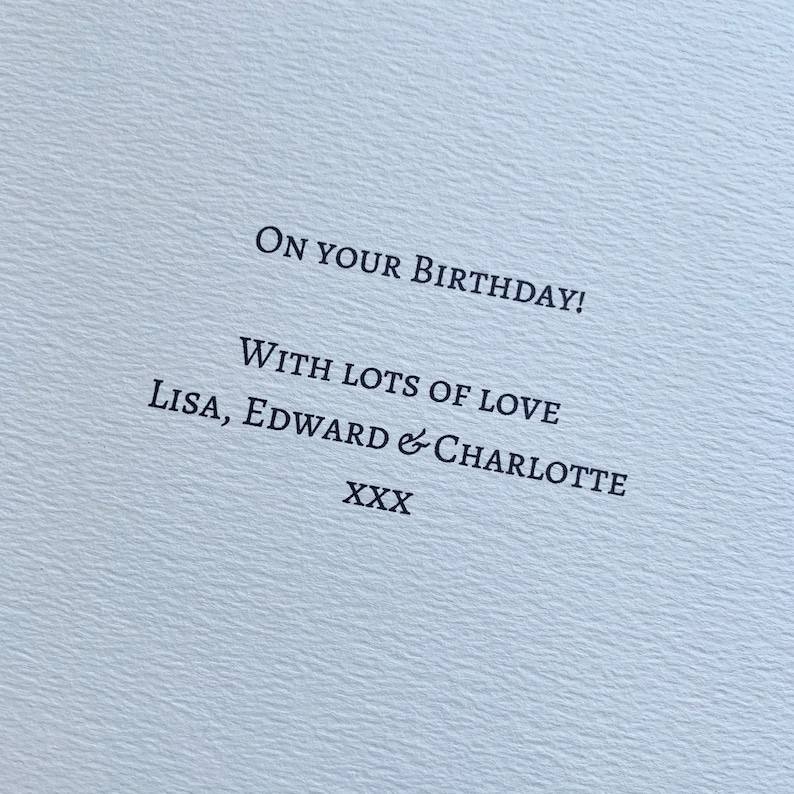 May include: A light blue card with the message "ON YOUR BIRTHDAY!" printed in black. The card also includes the text "WITH LOTS OF LOVE Lisa, Edward & Charlotte XXX". The card has a textured surface.