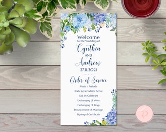 Op de afbeelding: Een trouwceremonie-volgordekaart met een aquarelbloemendesign met blauwe hortensia's en groene bladeren. De kaart heeft de tekst "Welkom op de bruiloft van Cynthia en Andrew 27.11.2021 Volgorde van de ceremonie" en somt de volgorde van de gebeurtenissen voor de ceremonie op.