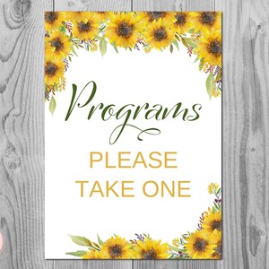 May include: A white sign with a sunflower border and the text "Programs Please Take One" in gold lettering.
