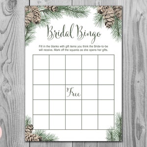 May include: A white Bridal Bingo game card with a pinecone and evergreen border. The card has a grid of squares with the word "Free" in the centre. The text "Bridal Bingo" is at the top.