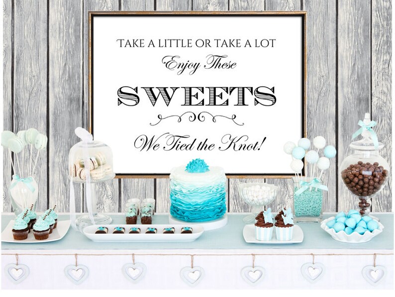 May include: A wedding dessert table with a sign that reads "Take a little or take a lot. Enjoy these sweets. We tied the knot!" The table is decorated with blue and white candy, cupcakes, cake pops, and a blue and white cake.
