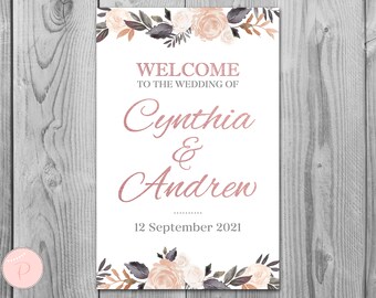 May include: A white wedding welcome sign with floral accents in shades of pink, brown, and gray. The text reads "Welcome to the wedding of Cynthia & Andrew 12 September 2021".