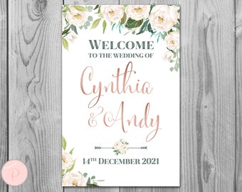 May include: A white wedding welcome sign with floral accents. The sign features the text "WELCOME TO THE WEDDING OF Cynthia & Andy" in a rose gold script font. The date "14th December 2021" is also displayed.