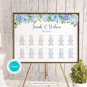May include: A framed wedding seating chart with blue floral accents. The chart lists names under table numbers 1-12. The names are in a simple font. The names "Sarah & Wilson" and the date "26th October" are at the top.