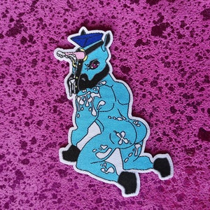 Op de afbeelding: Een blauwe eenhoorn met een politiepet en een witte kraag, met een roze hoorn en witte spetters op zijn lichaam. De eenhoorn knielt en heeft zijn hoofd naar de zijkant gedraaid.