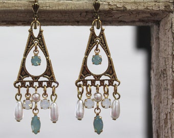 May include: A pair of gold tone dangle earrings with a triangular design. The earrings feature a light blue gemstone and white pearl accents.
