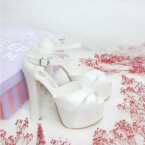 May include: White platform wedding shoes with a peep toe and ankle strap. The shoes have a high heel and are made of satin.