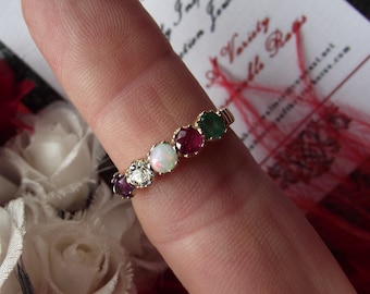 May include: A gold ring with a row of five gemstones. The gemstones are a purple stone, a diamond, a white opal, a ruby, and an emerald.