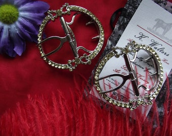May include: Two silver-toned metal buckles with clear rhinestone accents. The buckles are circular and have a decorative design. The buckles are on a red background with feathers.