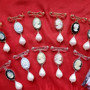 May include: Ten gold and silver tone brooches with cameo pendants and pearl drops. The cameos feature a variety of designs, including portraits and floral motifs. The brooches are perfect for adding a touch of vintage elegance to any outfit.