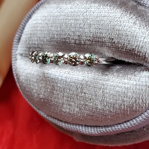 May include: A silver band ring with a row of small, round, green gemstones.