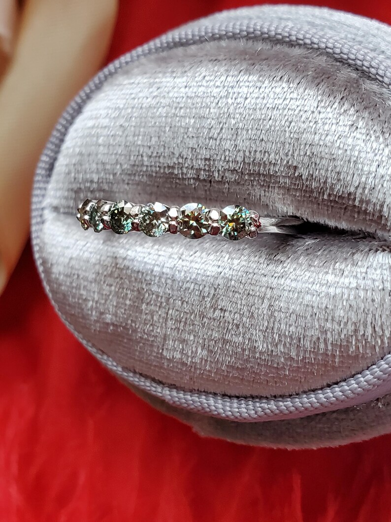 May include: A silver band ring with a row of small, round, green gemstones.