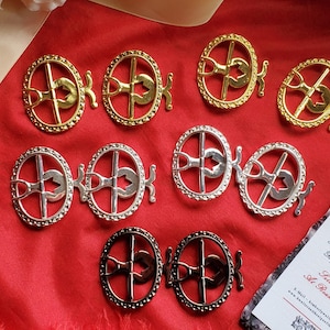 Pode incluir: Um conjunto de dez fechos metálicos decorativos em acabamentos prateado e dourado. Os fechos são circulares com uma barra transversal e um design em forma de coração no centro. Os fechos estão dispostos em duas filas de cinco, com os fechos dourados na parte superior e os fechos prateados na parte inferior.