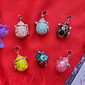 May include: Six different charm pendants with various colors and designs. The charms are in the shape of a small bottle, a strawberry, and a heart. The charms are made of metal and have a silver finish.