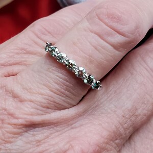 May include: A silver band ring with a row of small, clear, round gemstones.