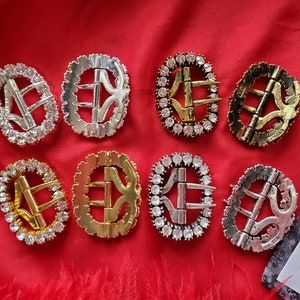 Puede incluir: Ocho hebillas metálicas ovaladas con adornos de strass transparentes. Las hebillas están en varios acabados, incluyendo plata, oro y latón antiguo.