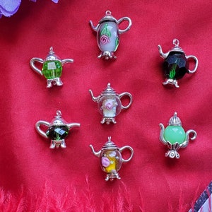 May include: Seven silver teapot charms with glass bodies. The charms feature different coloured glass and floral designs. The charms are perfect for adding a touch of whimsy to a jewellery collection.