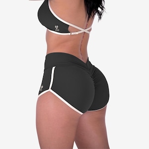 May include: Black athletic shorts and sports bra set with white trim. The shorts have a ruched back and a high waist. The sports bra has a criss-cross back design. Both pieces have a small logo on them.