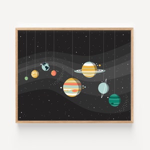 May include: A framed print depicting a stylised solar system with planets hanging from strings against a black background with white stars. The planets are in various colours, including orange, yellow, blue, green, and red.