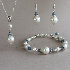 May include: A pearl and blue crystal jewelry set includes a necklace, earrings, and a bracelet. The necklace has a single pearl drop with a smaller pearl and crystal above it. The earrings have a single pearl drop with a crystal above it. The bracelet has alternating pearls and crystals.