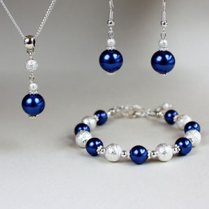 May include: A set of blue and silver jewelry featuring a necklace, earrings, and a bracelet. The necklace has a long pendant with a blue pearl and silver accents. The earrings are silver with blue pearls. The bracelet has alternating blue pearls and silver beads.