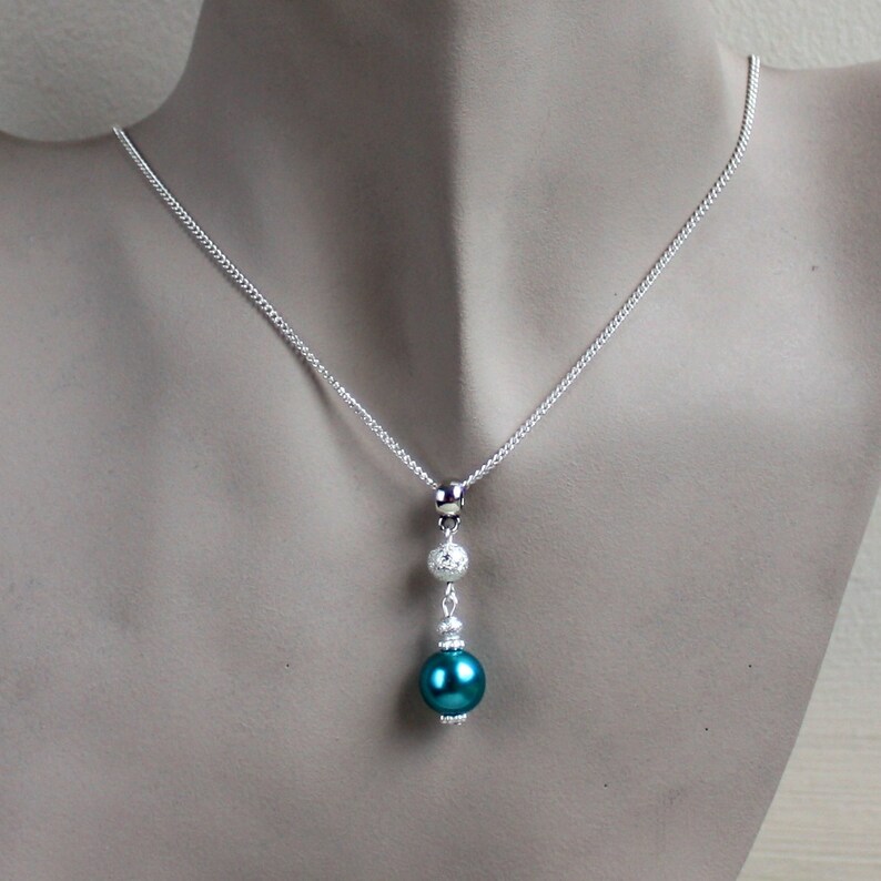 May include: A silver chain necklace with a teal pearl pendant and two silver beads.