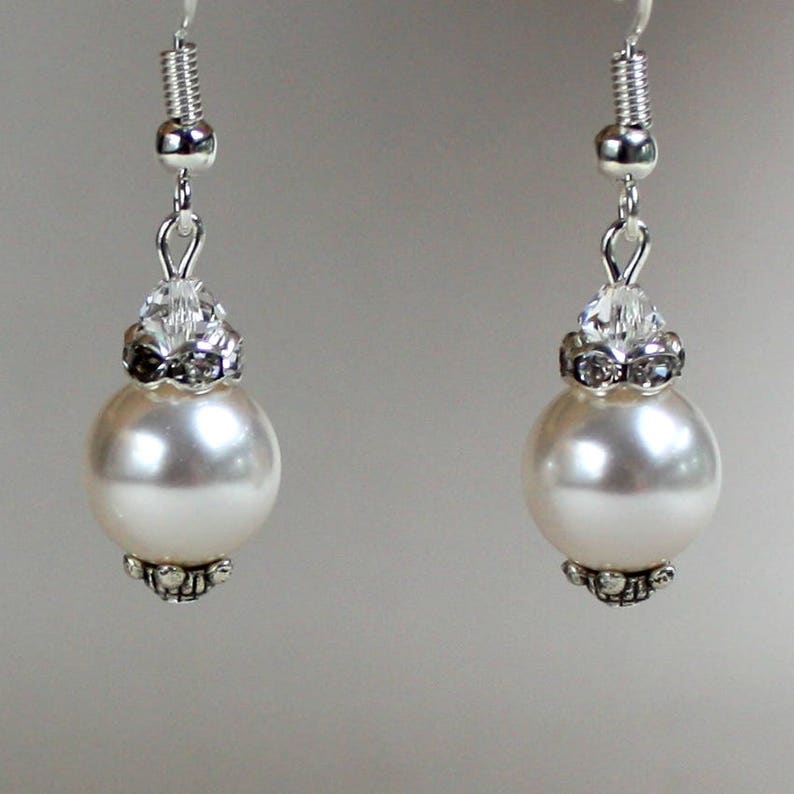 Peut inclure: Une paire de boucles d'oreilles en argent avec des perles blanches et des accents de cristal.