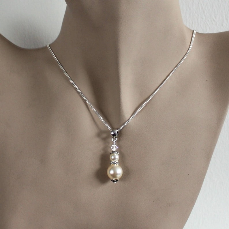May include: A silver chain necklace with a pendant featuring a single large cream-colored pearl and two smaller pearls accented with clear crystals.