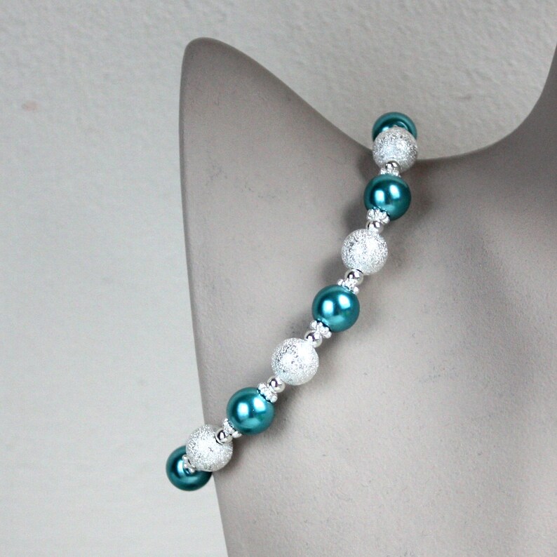 May include: A teal and silver beaded bracelet with alternating round beads. The silver beads have a textured surface.