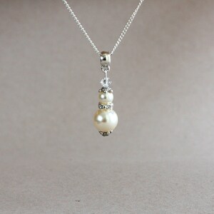 May include: A silver chain necklace with a pendant featuring two white pearls and a crystal accent.