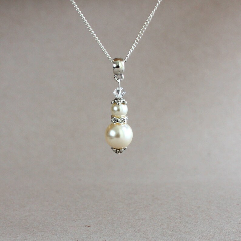 May include: A silver chain necklace with a pendant featuring two white pearls and a crystal accent.